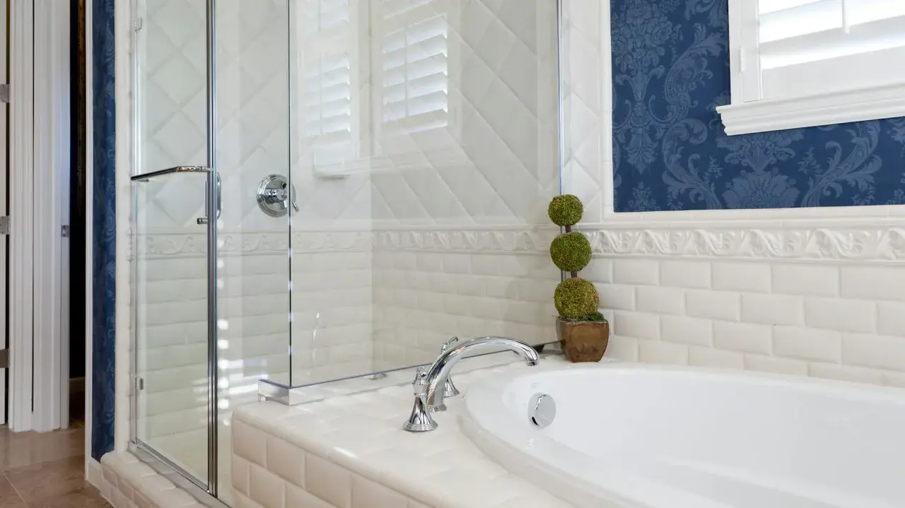 Elegantes Badezimmer mit Duschkabine, Wanne und blau gemusterter Tapete. Die weißen Fliesen und die Tapete ergeben ein stilvolles Ambiente.