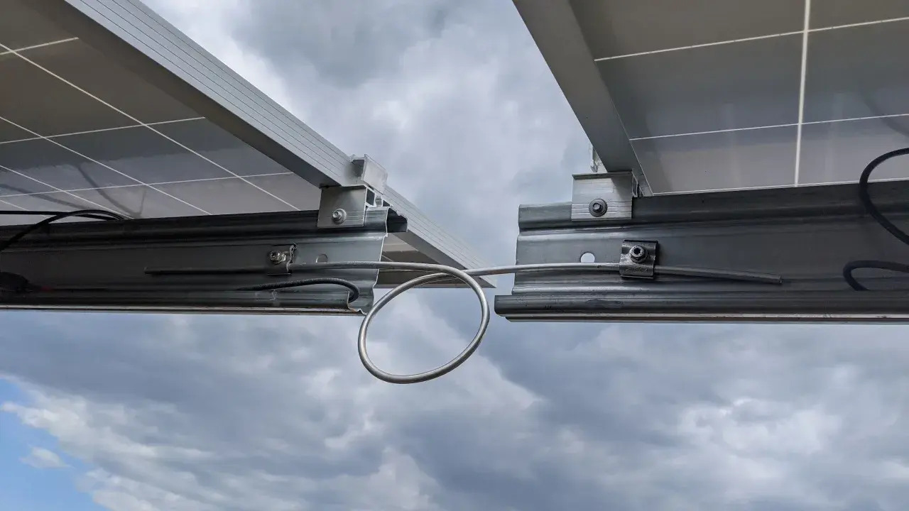 Detailaufnahme von Solarmodulen auf Montageschienen. Ein Kabel ist für die Erdung der PV-Schienen mit einer Schlaufe befestigt.