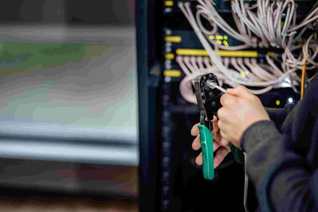 Person crimpt MC4 Stecker für Solarkabel. Im Hintergrund Server-Rack mit vielen Kabeln.