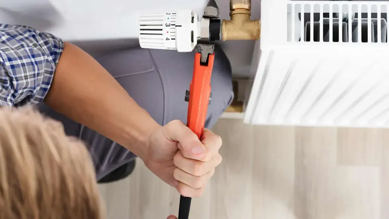Hand mit Rohrzange dreht am Heizkörperthermostat, um ihn abzuschrauben.