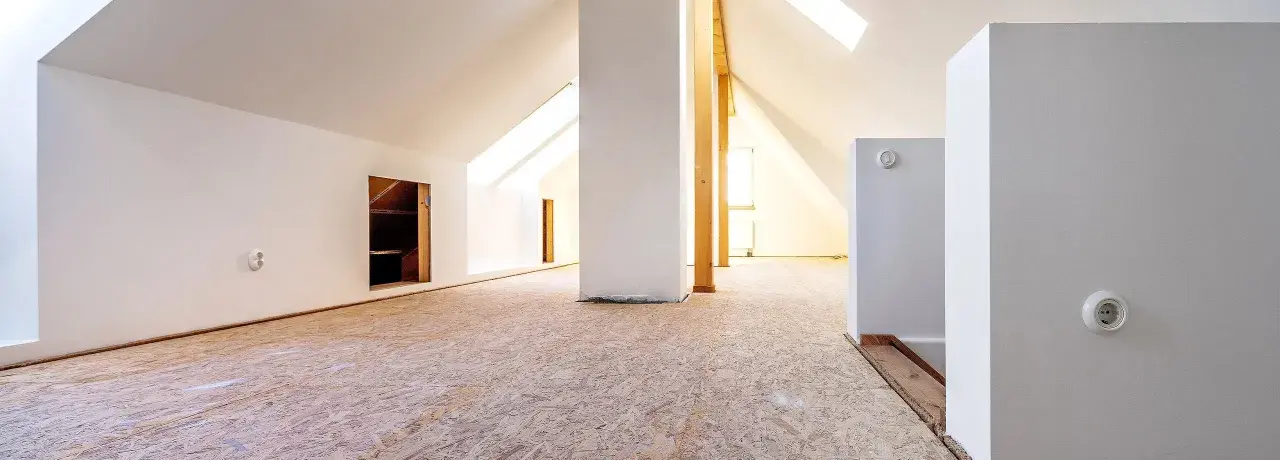 Blick in einen ausgebauten Dachboden mit OSB-Platten als Bodenbelag. Weiße Wände und Dachschrägen mit Fenstern.