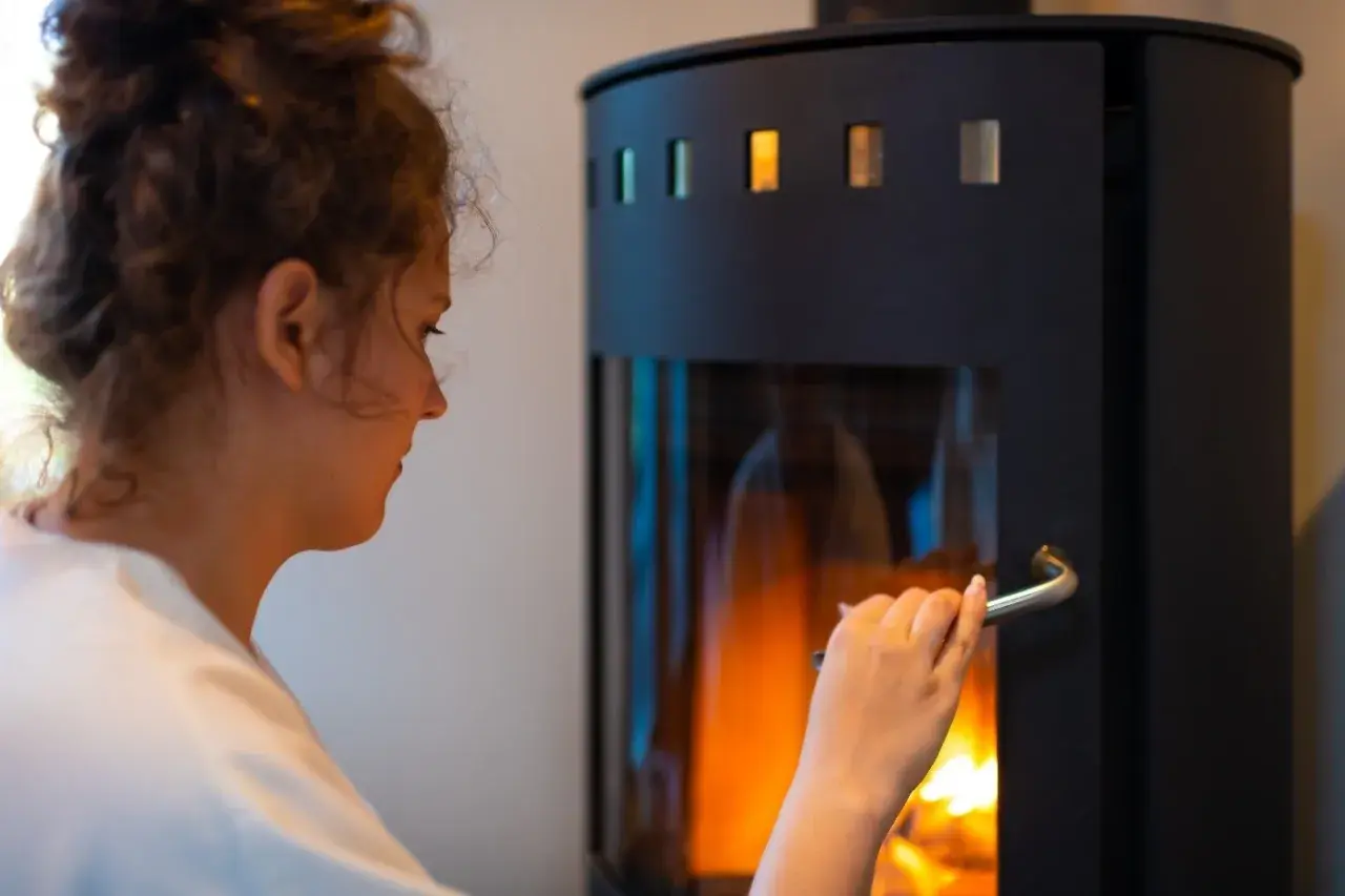 Frau öffnet Kamin. Die Drosselklappe des Ofenrohrs ist offen, um das Feuer zu speisen.