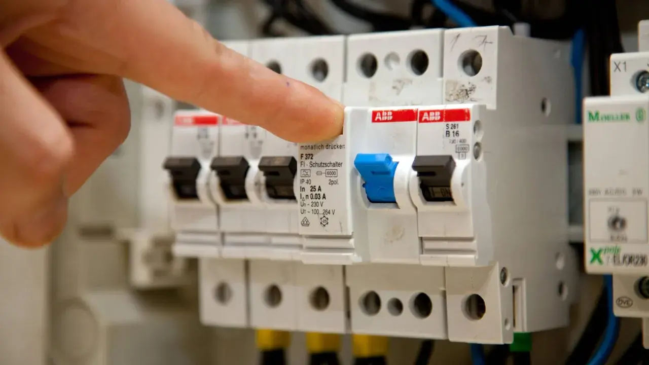 Finger betätigt eine elektrische Sicherung, einen FI-Schutzschalter, in einem Sicherungskasten.
