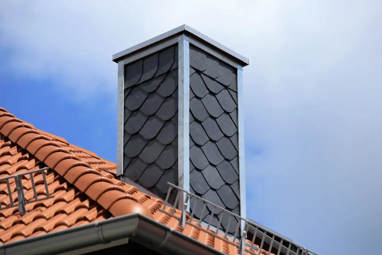 Moderner Schornstein mit Schieferplatten verkleidet, der die Schornstein verkleiden Vorschriften erf&uuml;llt. Dachziegel und Himmel im Hintergrund.