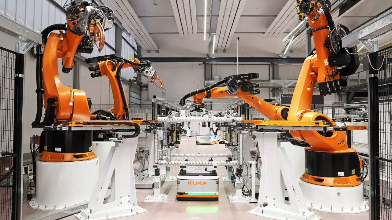 Industrielle Roboterarme in einer Fabrikhalle, bereit für ihre Instandhaltungsaufgaben. Kleine autonome Fahrzeuge bewegen sich zwischen den Stationen.
