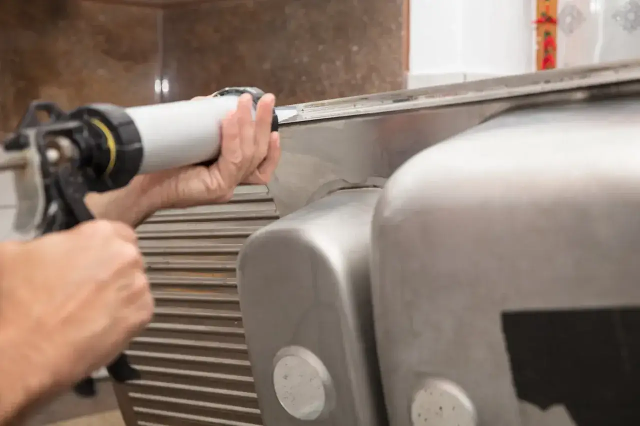 Hand mit Kartuschenpresse dichtet Sp&uuml;le ab. Der Unterschied zwischen Acryl und Silikon ist hierbei entscheidend f&uuml;r die Haltbarkeit.