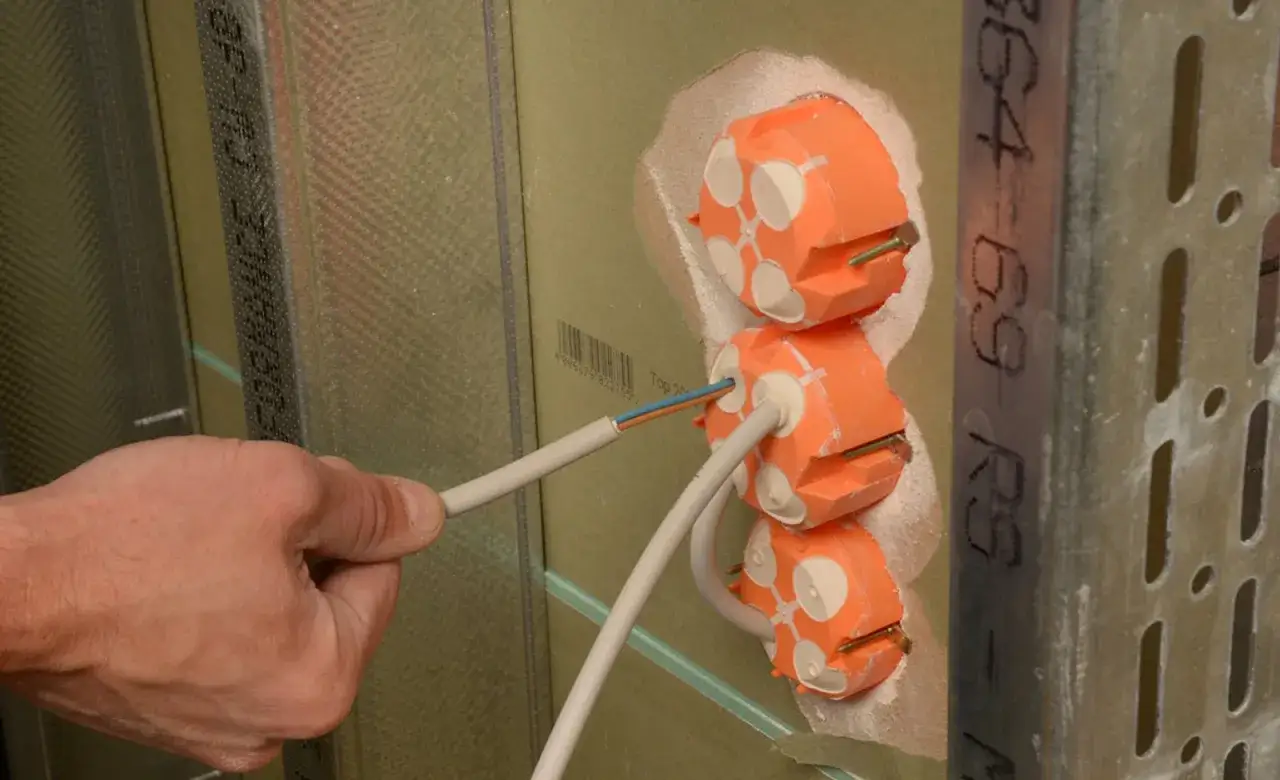 Elektroinstallation im Trockenbau: Ein Handwerker führt Kabel in orange Dosen ein. Beachtung der Vorschriften ist hierbei essenziell.
