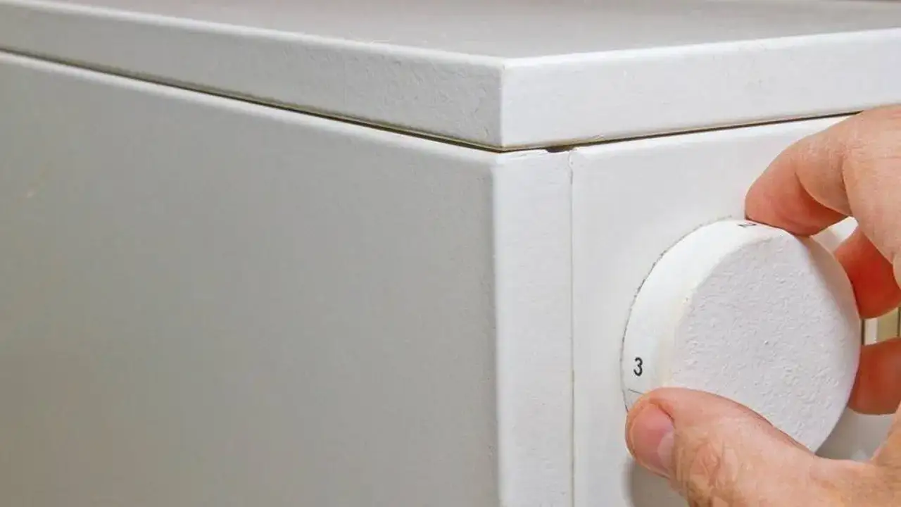 Hand dreht Regler an wei&szlig;er Nachtspeicherheizung. M&ouml;glicher Nachtspeicherheizung Verbot im Fokus.