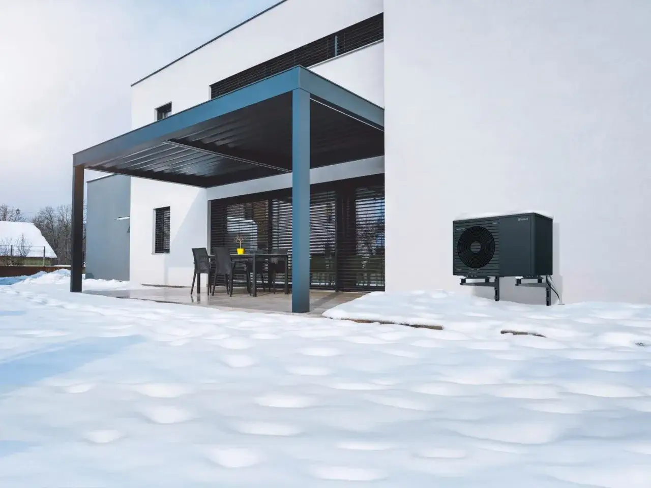 Moderne W&auml;rmepumpe vor einem Haus im Schnee. Sie fragt sich, wann werden Heizungen angestellt, um es warm zu halten.