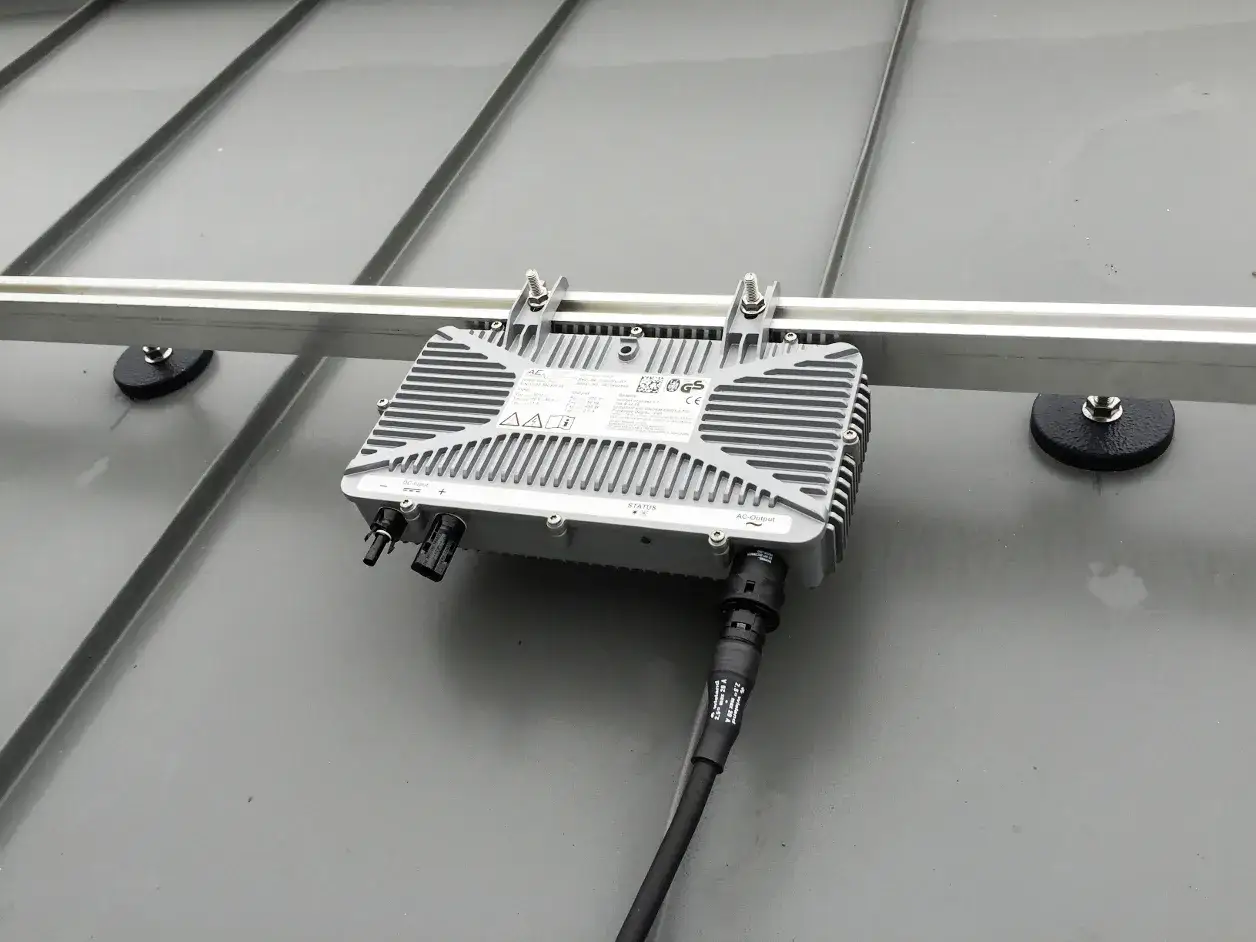 Ein Mikrowechselrichter wird auf einer Schiene montiert, die auf einem Metalldach befestigt ist.