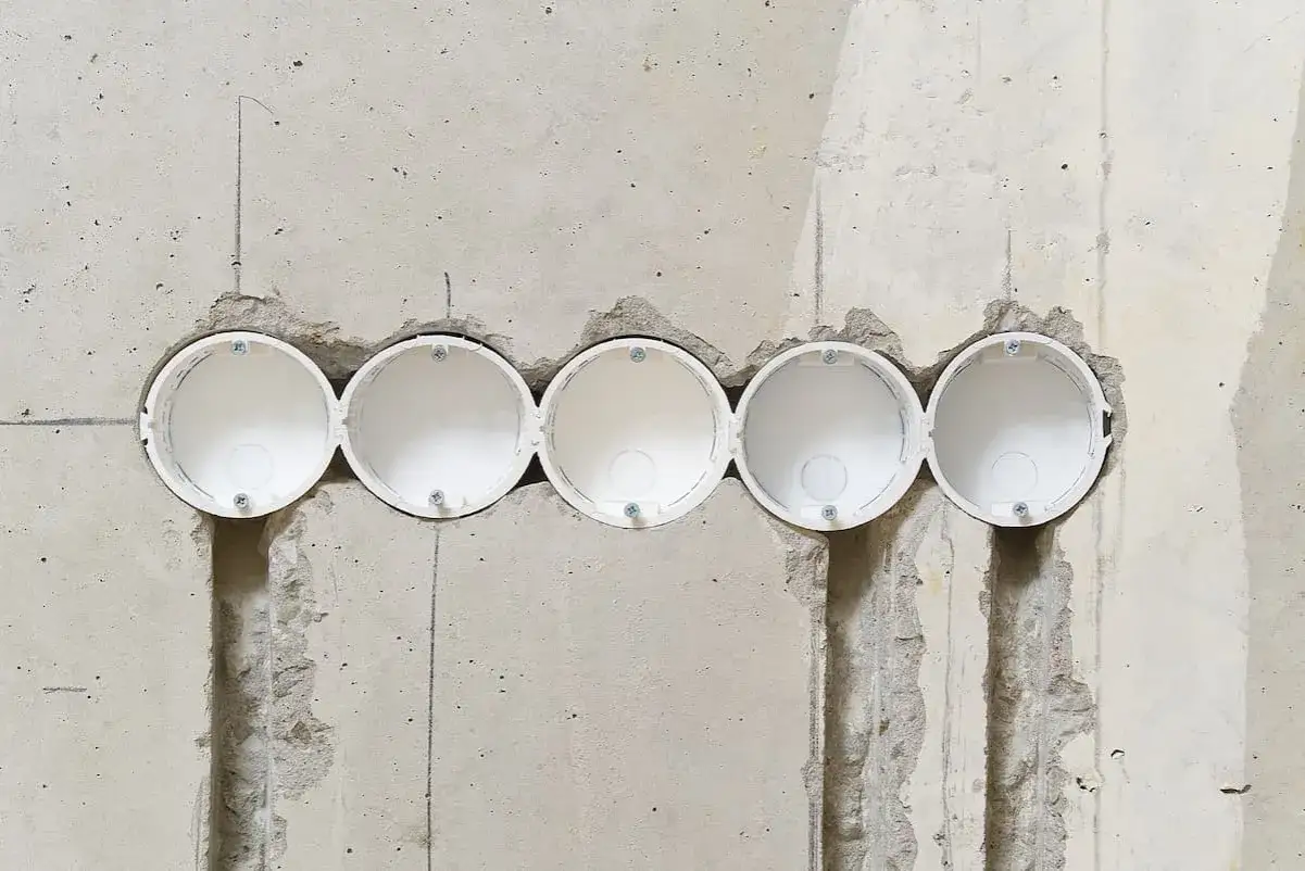 F&uuml;nf leere Unterputzdosen in einer Betonwand, bereit f&uuml;r die Installation. Der Abstand zwischen den Steckdosen betr&auml;gt 71 oder 72 mm.