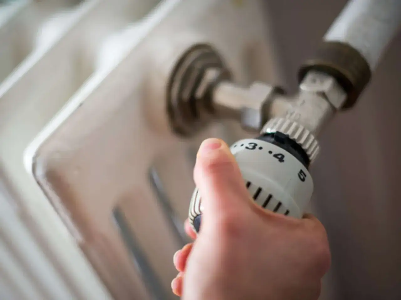 Hand dreht Thermostat am Heizkörper, um zu verhindern, dass Heizungsrohre einfrieren.