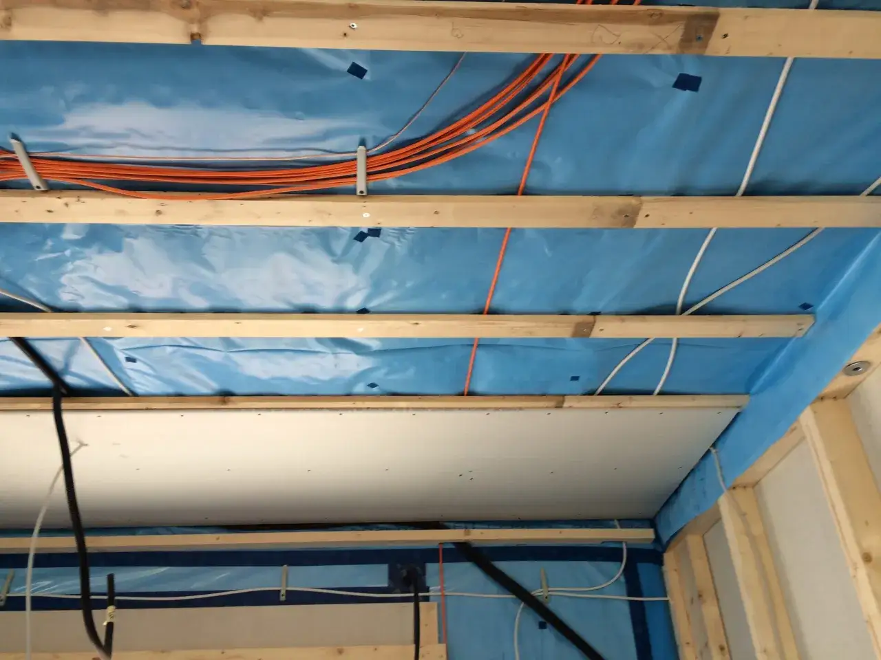 Holzbalken und Dampfsperre f&uuml;r die Befestigung von schweren Lasten an Rigipsdecke. Orange Kabel und wei&szlig;e Leitungen verlaufen darunter.