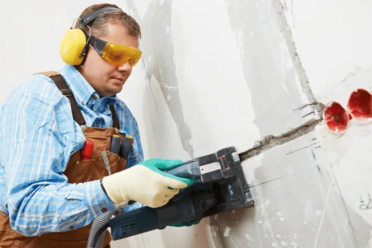 Handwerker mit Schutzbrille und Geh&ouml;rschutz schlitzt mit einer Maschine eine Wand, um Kabel zu verlegen.