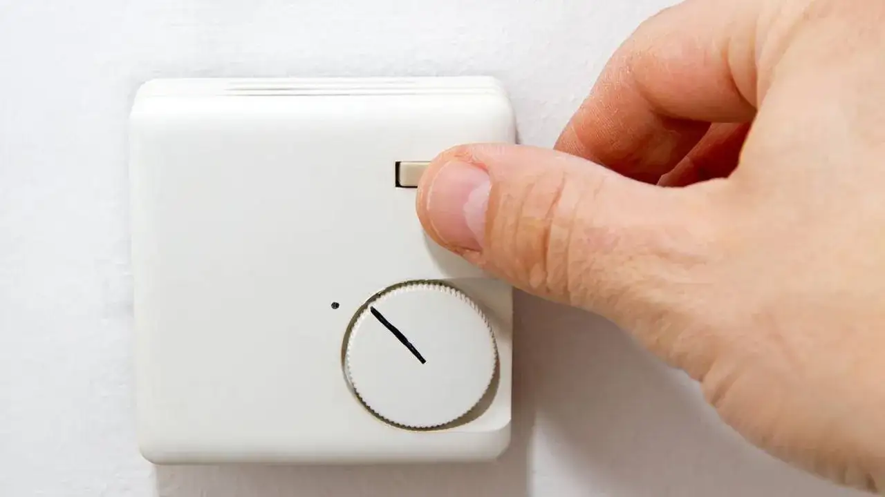 Hand dreht am Regler einer alten Nachtspeicherheizung zur Bedienung.