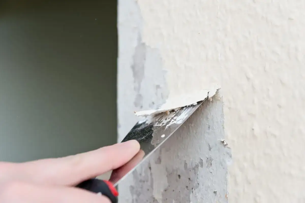 Mit einem Spachtel wird alte vliestapete auf raufaser entfernt.