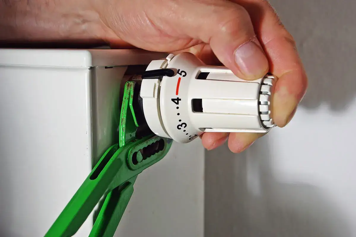 Hand dreht mit Zange den Thermostatkopf ab, um ihn zu wechseln.