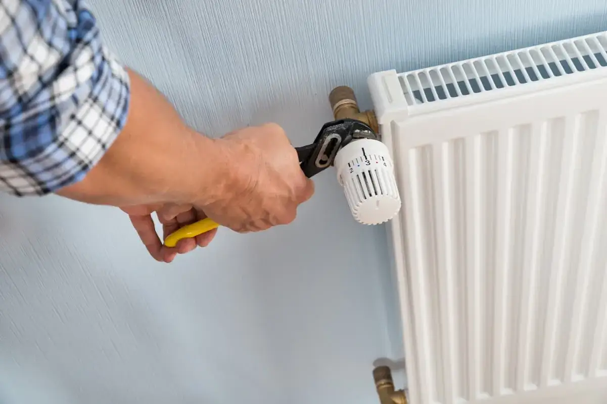 Hand mit Zange dreht am Heizk&ouml;rperthermostat, um ihn abzuschrauben.