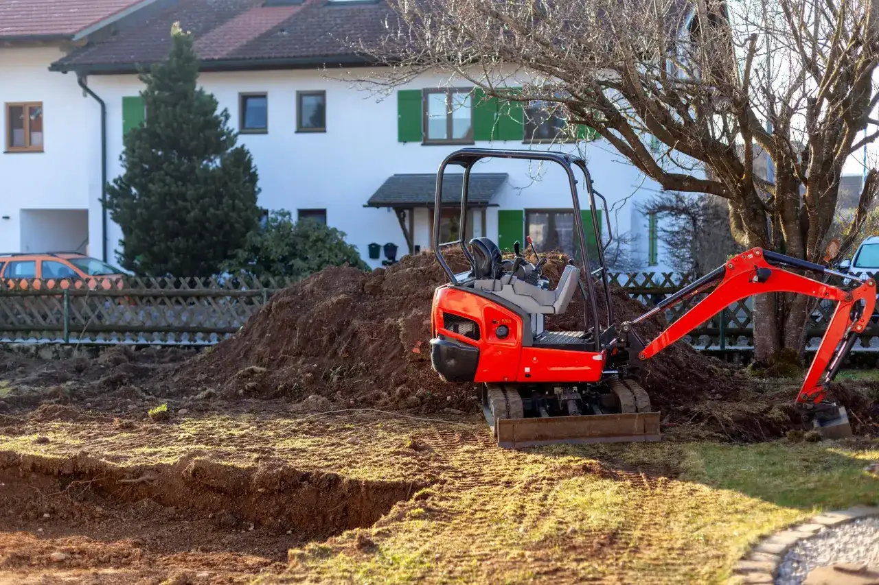 Kleiner Bagger neben einem Haufen Erdreich aus einer Baugrube.